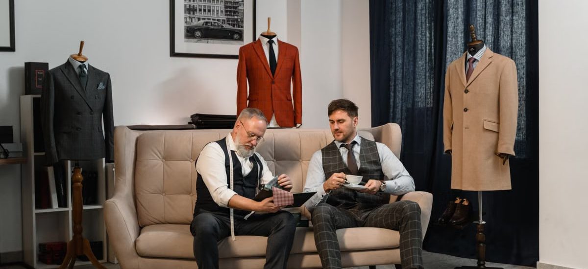 Two tailors in a stylish workshop discussing custom suit designs surrounded by elegant suits.